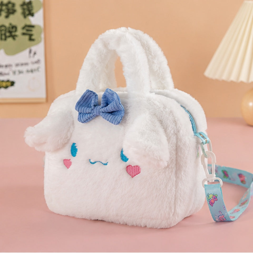 une petite sacoche toute douce et fluffy de Cinnamoroll. Elle est blanche et les yeux et des coeurs roses sont brodés dessus et arbore un joli noeud bleu. Elle est de côté dans une pièce rose.