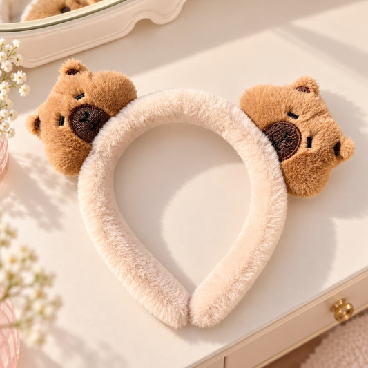 Serre-tête kawaii en peluche beige toute douce, orné de deux adorables têtes de capybaras marron aux petites bouilles attendrissantes. Posé à plat sur une jolie coiffeuse crème, avec quelques fleurs blanches et une décoration délicate. Un accessoire pour cheveux original, moelleux et mignon, idéal pour les amoureuses de capybaras et de mode kawaii.
