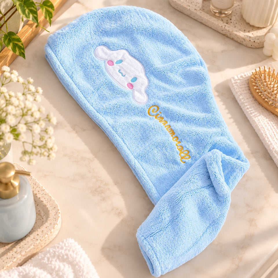 Serviette pour cheveux Cinnamoroll bleu clair en tissu doux, posée à plat dans un joli décor de salle de bain lumineux avec accessoires de soin et fleurs.