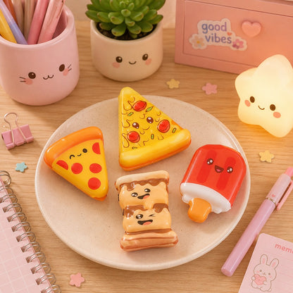 Des squishies anti-stress kawaii en forme de part de pizza classique, une part de pizza au pepperoni, une glace à l'eau rouge et une guimauve au chocolat, tous avec de petits visages souriants., disposés sur une assiette beige posée sur un bureau en bois clair. Autour de l'assiette se trouvent des accessoires de papeterie pastel créant une ambiance douce, chaleureuse et mignonne