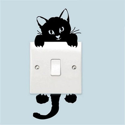 un sticker mural d'un chat noir très mignon et espiègle Il est divisé en deux parties : une supérieure à coller au-dessus d'un interrupteur et la partie inférieure en dessous. Il ajoute une touche mignonne à une pièce.