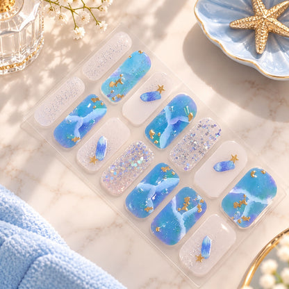Stickers nail art bleu et blanc à paillettes avec motifs marins et détails dorés, présentés dans un élégant décor beauté aux tons bleu pastel.