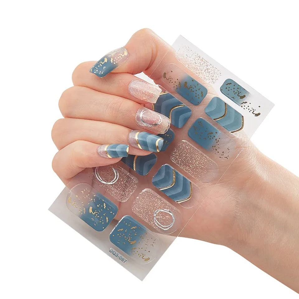 Stickers nail art légèrement transparents bleu canard et rose pailleté, décorés de détails dorés et argentés, tenus dans une main dont les ongles portent ces stickers.