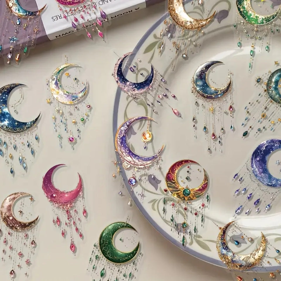 des stickers en forme de lune coloré et décorées de détails dorés, des pampilles et strass colorés et brillantes y sont suspendus