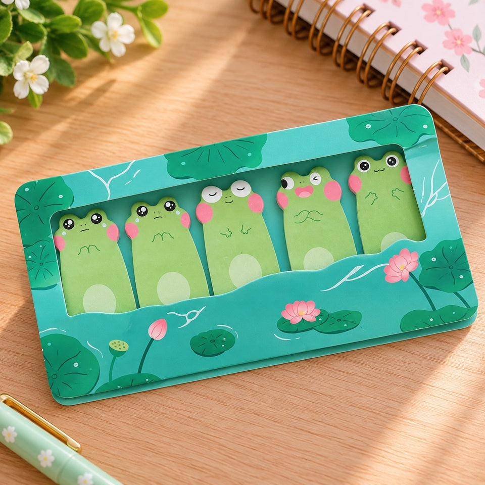 Lot de 5 mémos adhésifs kawaii en forme de grenouilles vertes aux expressions rigolotes, dans un étui turquoise décoré de nénuphars et fleurs de lotus roses, posé sur un bureau en bois clair avec accessoires de papeterie.