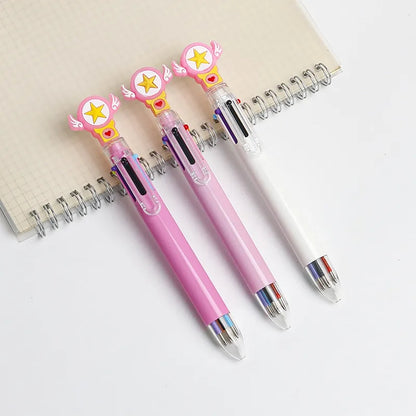 Trois stylos multicolores kawaii rose foncé, rose pastel et blanc, ornés d’une étoile jaune et de petites ailes, présentés sur un carnet posé sur un joli bureau blanc.