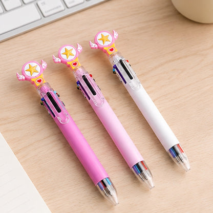 Trois stylos multicolores kawaii rose foncé, rose pastel et blanc, ornés d’une étoile jaune et de petites ailes, présentés sur un carnet posé sur un joli bureau en bois clair.