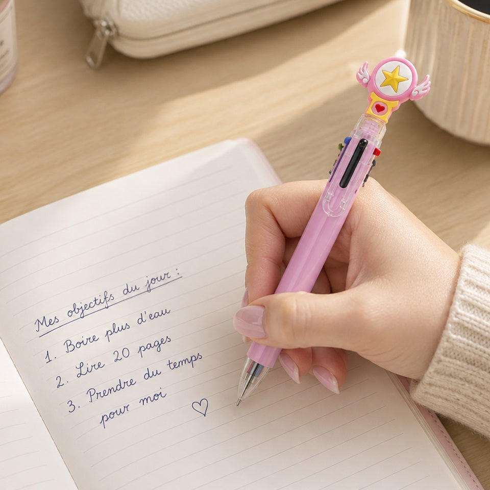 Stylo multicolore kawaii rose avec étoile et petites ailes, tenu par une femme écrivant en français dans un joli carnet sur un bureau lumineux et élégant.