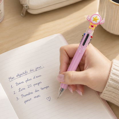 Stylo multicolore kawaii rose avec étoile et petites ailes, tenu par une femme écrivant en français dans un joli carnet sur un bureau lumineux et élégant.