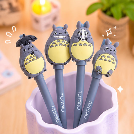 Lot de 4 stylos gel Totoro kawaii gris avec personnages inspirés de l’univers japonais, présentés dans un pot pastel violet sur un bureau chaleureux aux tons doux et mignons.
