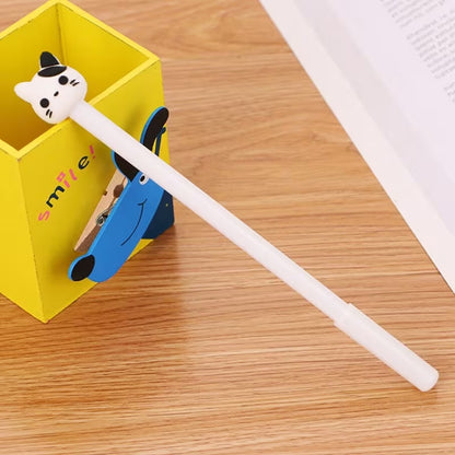 Un stylo blanc dont le bout est une tête de chat noir et blanche présenté sur un bureau clair. Design mignon et fun.
