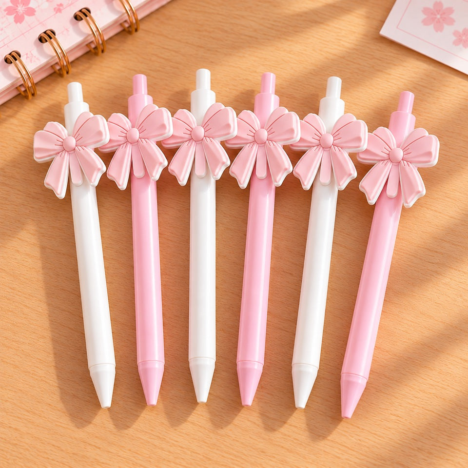Six stylos kawaii élégants, roses et blancs, ornés de grands nœuds en relief assortis, disposés sur un bureau en bois clair. Ces adorables stylos au style chic, romantiques sont trop mignons.