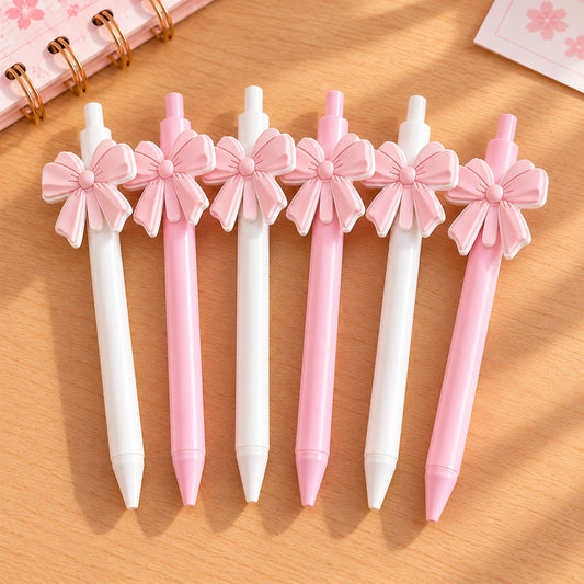 Six stylos kawaii élégants, roses et blancs, ornés de grands nœuds en relief assortis, disposés sur un bureau en bois clair. Ces adorables stylos au style chic, romantiques sont trop mignons.