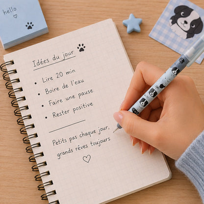 un stylo de couleur bleu au motif de chiens noirs tenu dans une main de femme. Elle écrit sur un journal des notes.