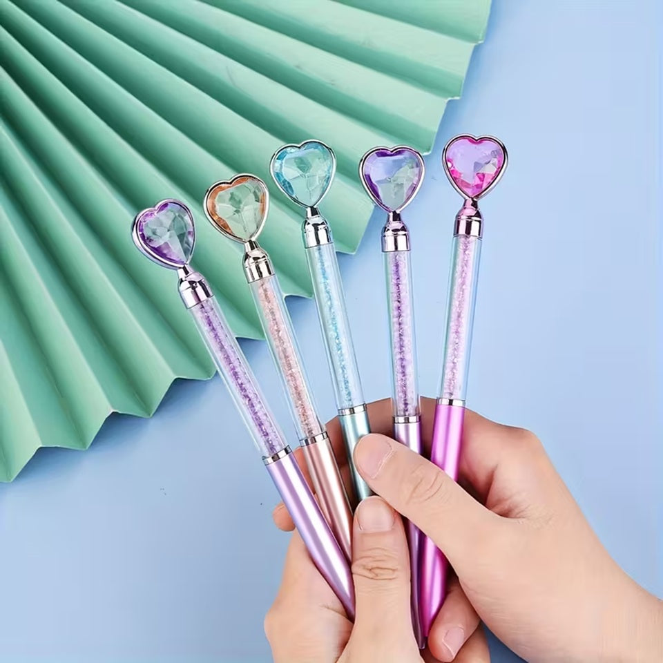 des stylos coeurs colorés dont le corps transparent renferme des strass brillants. Au but du stylo se trouve un joli coeur coloré comme s'il avait été taillé dans un diamant. L'ensemble est poétique et élégant.
