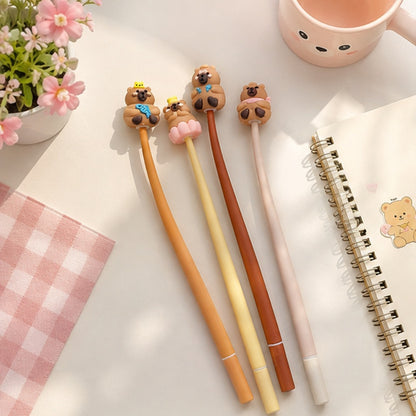 Stylos capybara souples kawaii disposés sur un carnet dans un joli décor pastel avec fleurs et tissu à carreaux roses. Lot de 4 stylos fantaisie mignons pour papeterie, école et bureau.