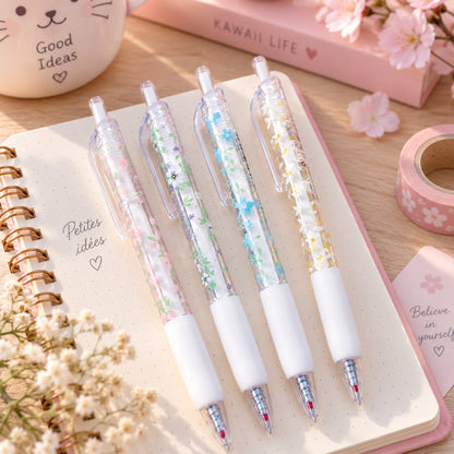 Lot de quatre stylos transparents à motifs de petites fleurs colorées, présentés sur un carnet dans un décor de papeterie doux et fleuri.