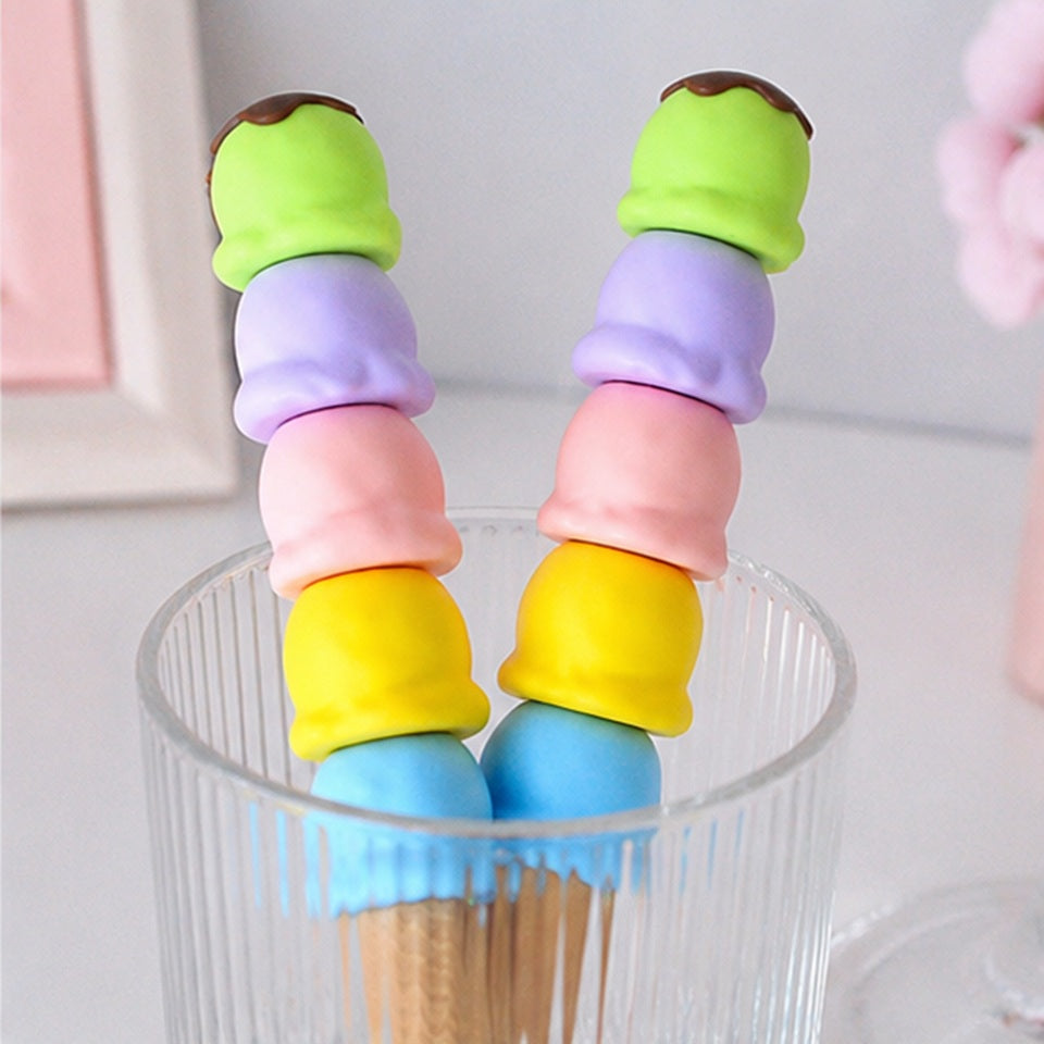 Gros plan sur des surligneurs en forme de glaces pastel présentés sur une assiette blanche à bord festonné. Les embouts jaune et violet sont ouverts pour révéler leurs pointes, tandis que le capuchon bleu en forme de cornet est posé à côté. L'ensemble est photographié dans une ambiance douce et lumineuse, avec une esthétique kawaii aux tons pastel.