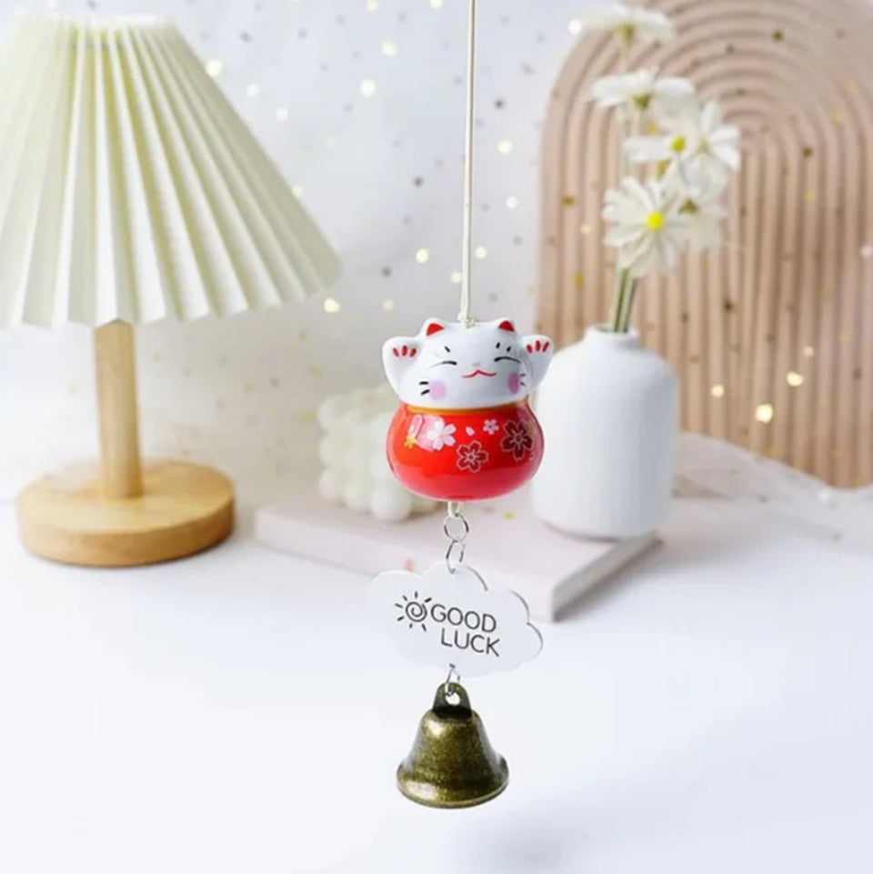des suspensions en forme de maneki neko rouge, rose ou bleu. Une clochette y est suspendue avec une petite plaque décorative. Les maneki neko ont les pattes levées et des fleurs de sakura sur le ventre