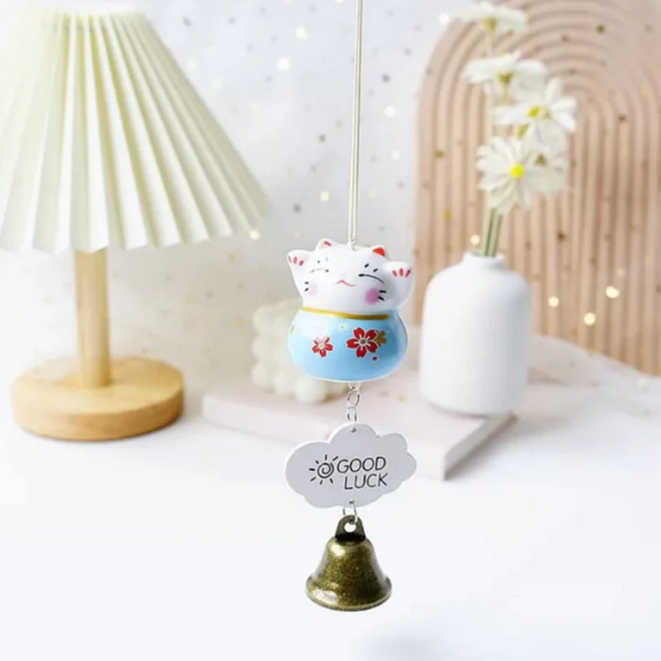 des suspensions en forme de maneki neko rouge, rose ou bleu. Une clochette y est suspendue avec une petite plaque décorative. Les maneki neko ont les pattes levées et des fleurs de sakura sur le ventre