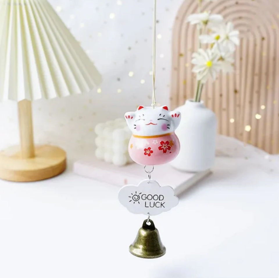 des suspensions en forme de maneki neko rouge, rose ou bleu. Une clochette y est suspendue avec une petite plaque décorative. Les maneki neko ont les pattes levées et des fleurs de sakura sur le ventre
