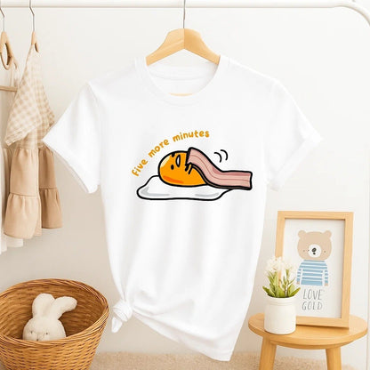 un tee-shirt blanc sur lequel est représenté Gudetama, l'oeuf mignon et rigolo de Sanrio. Il est recouvert d'une tranche de bacon comme une couverture avec le message suivant : encore 5 minutes de plus.