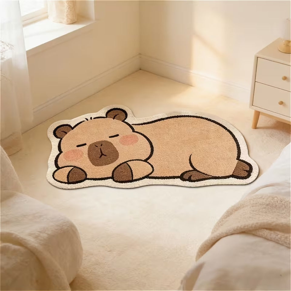 Un tapis de sol en forme et aux couleurs d'un adorable capybara. Il est couché et semble dormir paisiblement. Il est posé dans le coin d'une chambre créant une ambiance douce et calme.