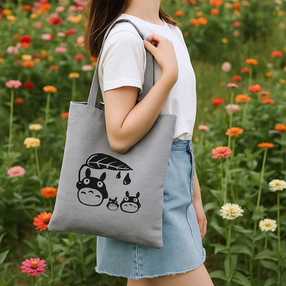 un joli tote bag gris illustré de Totoro et de ses amis en version chibi. Il porte une feuille au-dessus de lui.