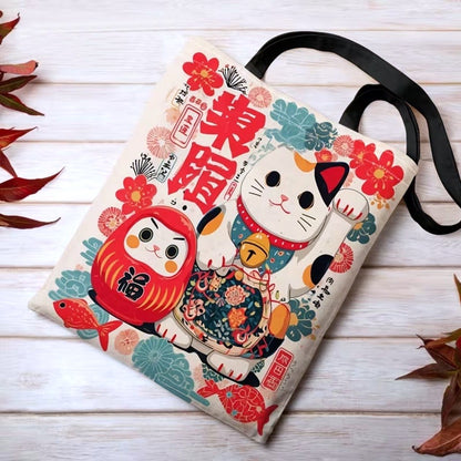 Tote bag japonais illustré d'un Maneki Neko et d'un Daruma dans des tons rouge, vert et bleu. Sac en tissu au design kawaii inspiré des porte-bonheurs traditionnels du Japon.