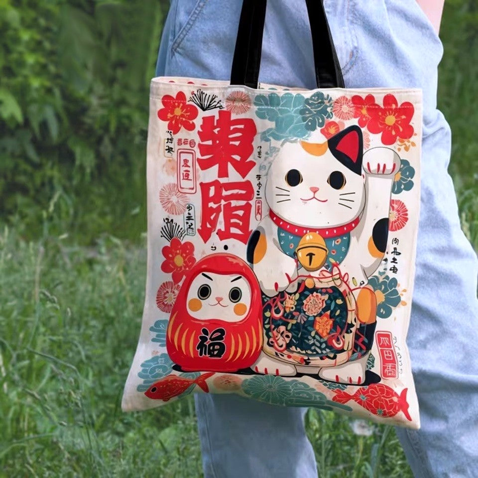 Tote bag japonais illustré d'un Maneki Neko et d'un Daruma dans des tons rouge, vert et bleu. Sac en tissu au design kawaii inspiré des porte-bonheurs traditionnels du Japon.