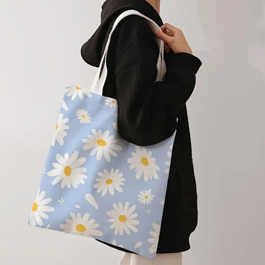 un tote bag en polyester au motif de marguerites blanches sur un fond bleu ciel. Avec ses deux anses blanches, il est pratique pour transporter tous les essentiels.