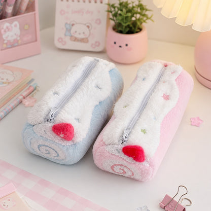 Deux trousses en peluche kawaii, l'une rose pastel et l'autre bleu pastel, sont posées côte à côte sur un joli bureau aux tons doux. Autour d'elles se trouvent des stylos, un carnet illustré, un pot de fleurs, une lampe d'ambiance et de petits accessoires décoratifs roses et blancs. L'ensemble crée une atmosphère chaleureuse, féminine et mignonne, idéale pour une présentation de fournitures de papeterie