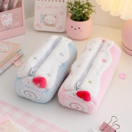 Deux trousses en peluche kawaii, l'une rose pastel et l'autre bleu pastel, sont posées côte à côte sur un joli bureau aux tons doux. Autour d'elles se trouvent des stylos, un carnet illustré, un pot de fleurs, une lampe d'ambiance et de petits accessoires décoratifs roses et blancs. L'ensemble crée une atmosphère chaleureuse, féminine et mignonne, idéale pour une présentation de fournitures de papeterie