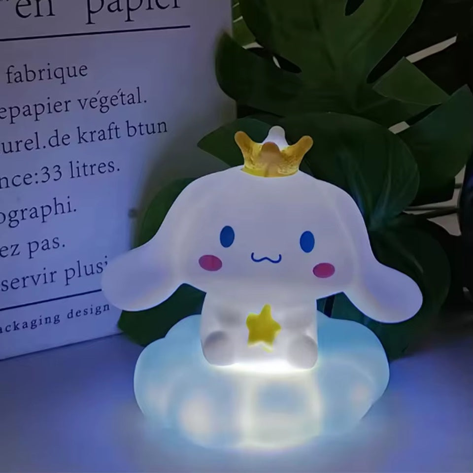 une adorable veilleuse cinnamoroll qui tient une étoile dans ses mains et qui porte une couronne jaune sur la tête. Il est assis sur un petit nuage. C'est une scène tendre. Elle diffuse de la lumière douce pour créer un effet cocooning.