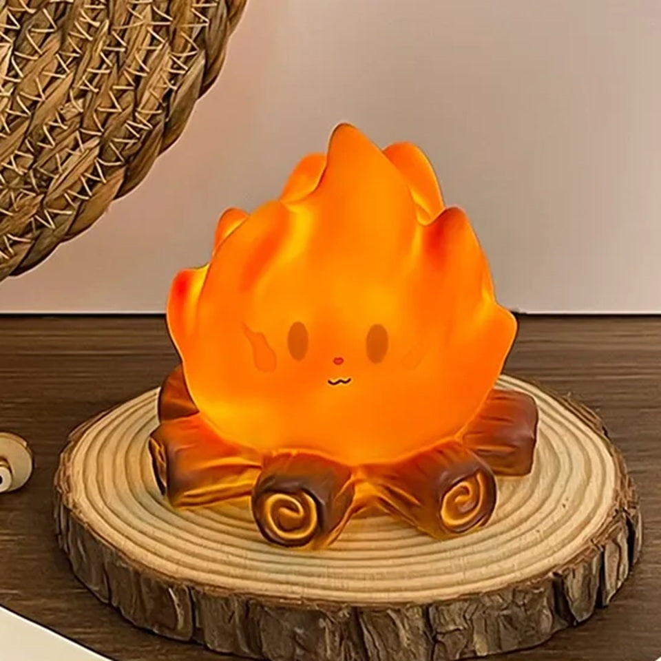 une petite veilleuse adorable en forme d'un feu de camp avec ses buches et sa grosse flamme au visage expressif kawaii est posée sur un petit rondin de bois sur une table en chêne.